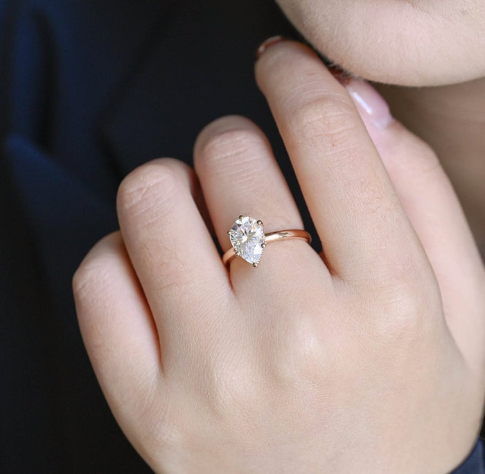 Pear shaped moissanite solitaire engagement ring held by five small ball tipped claws on a slim polished rose gold band, view 2