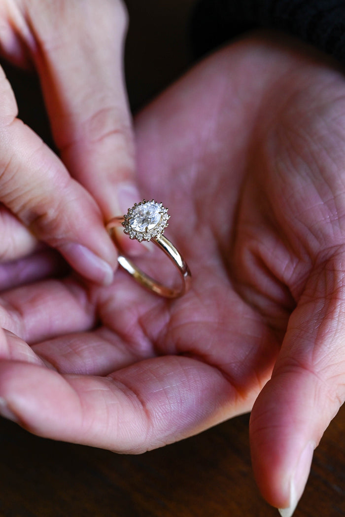 Oval moissanite floral halo engagement ring with a ring of small claw set round stones around the oval on a slim polished yellow gold band, view 2