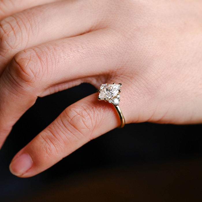 Marquise cut moissanite cluster engagement ring with a trio of round stones on each side on a plain yellow gold band, view 2
