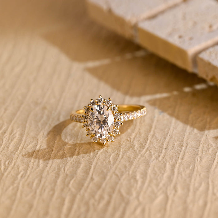 Oval moissanite sunburst halo engagement ring with pointed prong tips around the halo and a pave set yellow gold band