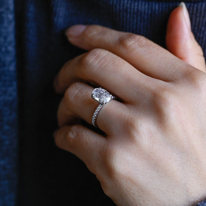 Elongated oval moissanite tulip set engagement ring with four claws on a slim white gold band set with small round stones, view 2