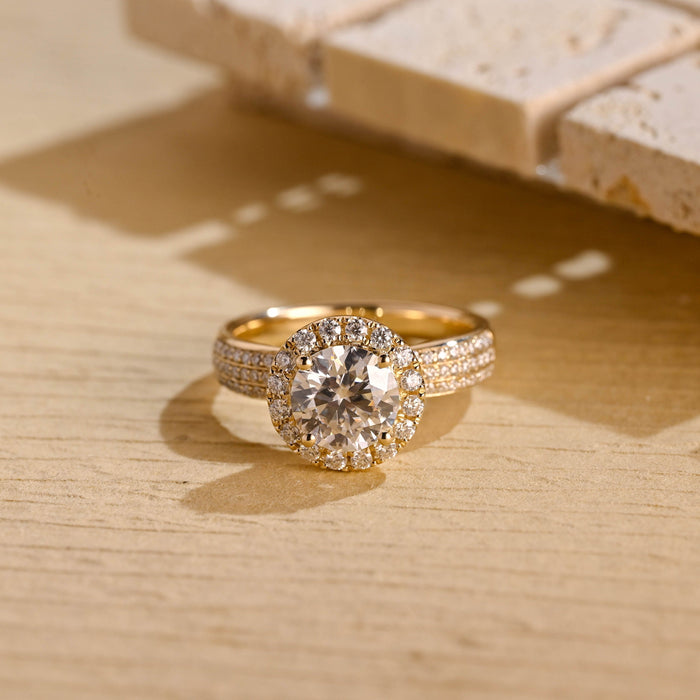 Round moissanite halo engagement ring with four claws and a wide yellow gold band pave set with three rows of small round stones