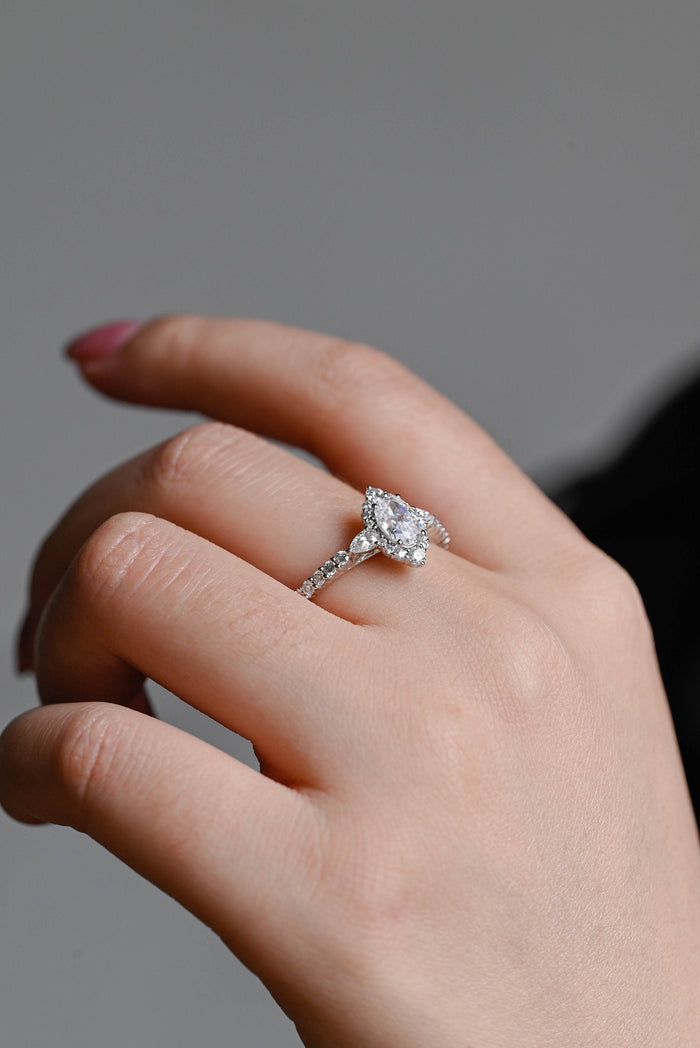 Oval moissanite vintage style halo engagement ring with a pointed halo, a pear shaped stone on each side and a pave set white gold band, view 2