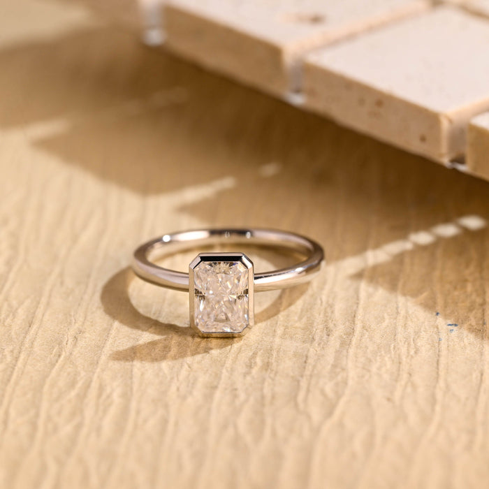 Bezel set radiant cut moissanite solitaire engagement ring on a plain polished white gold band