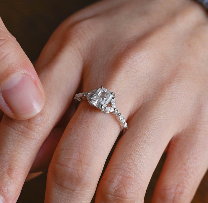 Radiant cut moissanite engagement ring with pairs of marquise stones at each side and a band set with alternating round and marquise stones in white gold, view 2