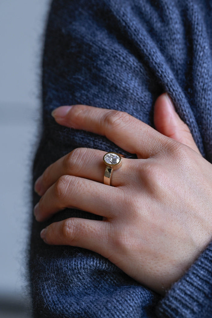 Oval moissanite bezel set solitaire engagement ring on a wide flat polished yellow gold band, view 2