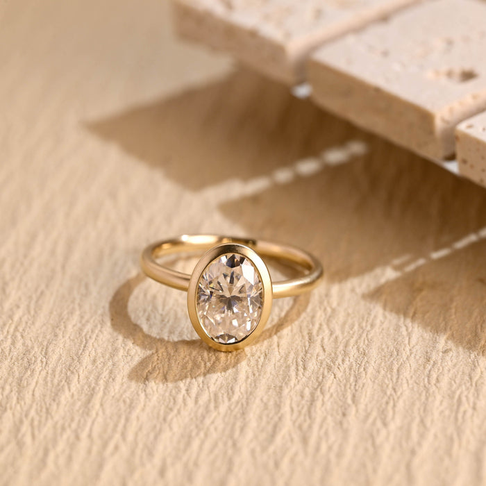 Oval moissanite bezel solitaire engagement ring with a soft matte finish on a slim round yellow gold band