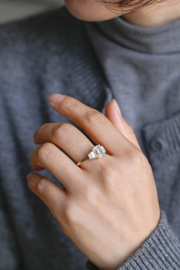 Emerald cut moissanite five stone engagement ring with two stepped baguettes on each side of a slim yellow gold band, view 2