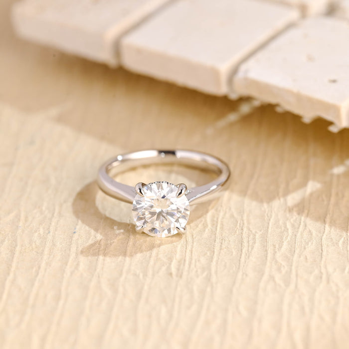 Round moissanite hidden halo engagement ring in four claws on a smooth polished white gold band that tapers up to the stone