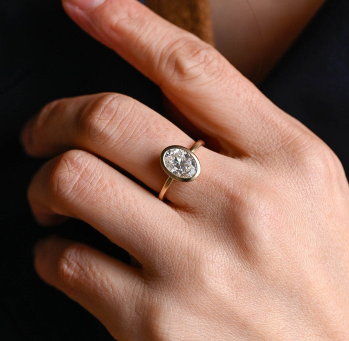 Oval moissanite bezel solitaire engagement ring with a soft matte finish on a slim round yellow gold band, view 2