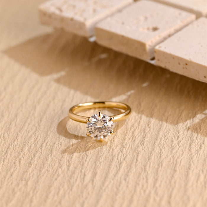 Round moissanite statement solitaire engagement ring on six slender claws above a smooth rounded yellow gold band