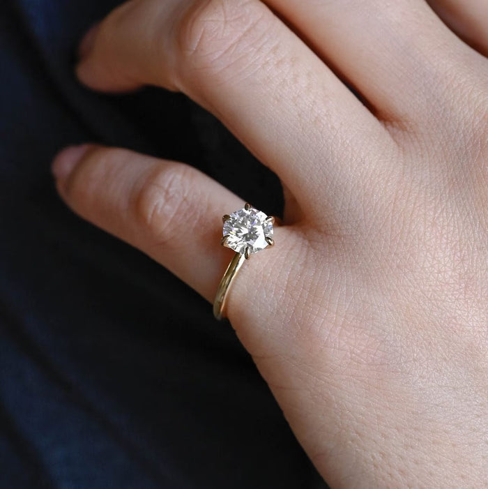 Round moissanite statement solitaire engagement ring on six slender claws above a smooth rounded yellow gold band, view 2