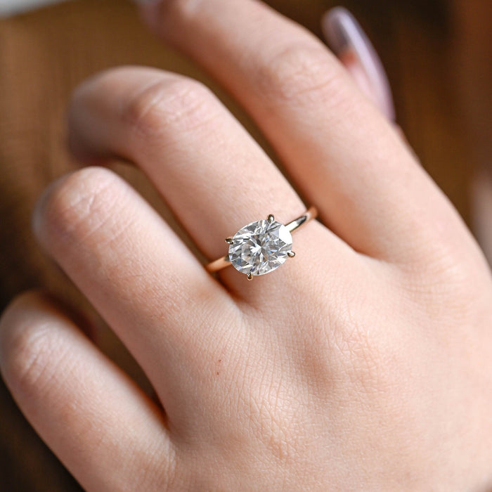 East west oval moissanite solitaire engagement ring set sideways in four slim claws on a slim polished yellow gold band, view 2