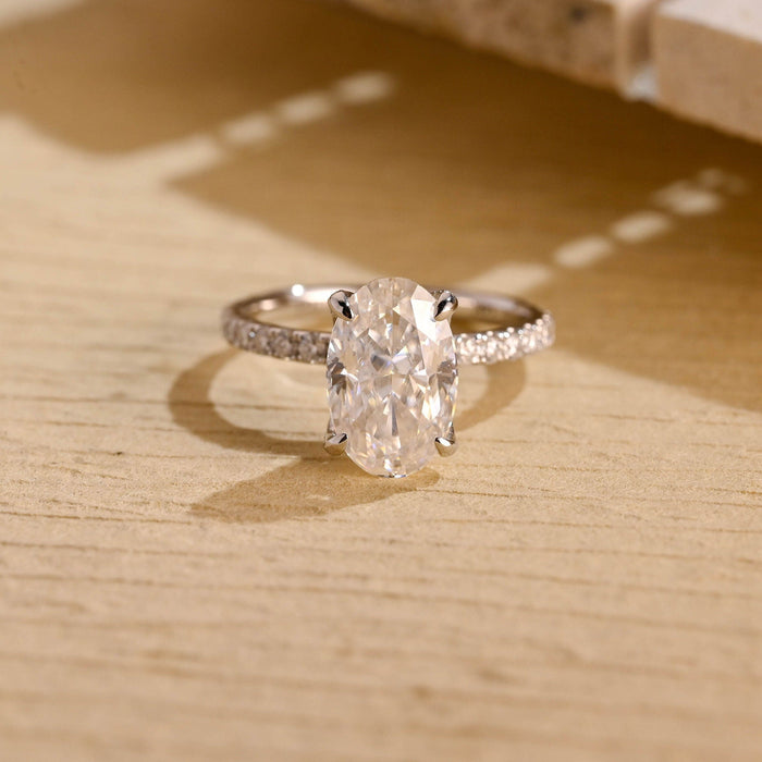 Elongated oval moissanite tulip set engagement ring with four claws on a slim white gold band set with small round stones