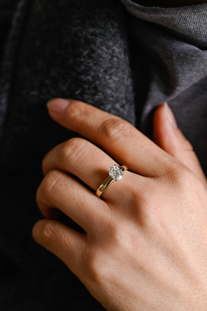 Oval moissanite solitaire engagement ring held by four slim claws on a broad domed polished yellow gold band, view 2
