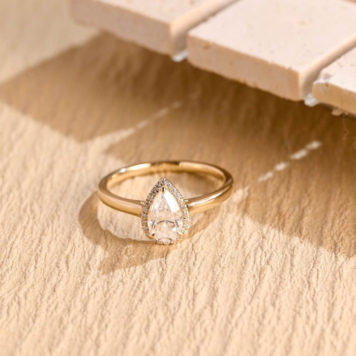 Pear shaped moissanite halo engagement ring with a teardrop halo of tiny round stones on a slim tapered polished yellow gold band
