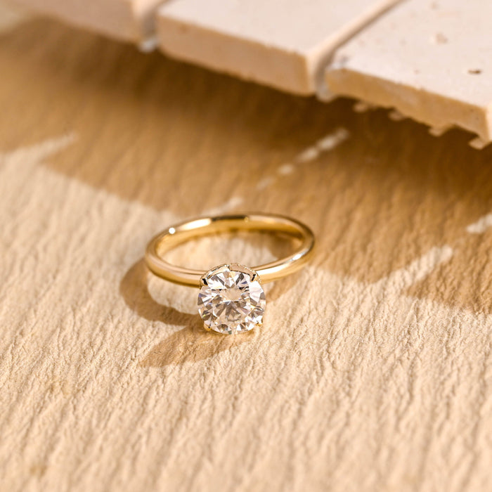 Round moissanite hidden halo engagement ring held by six slim claws on a slim polished yellow gold band
