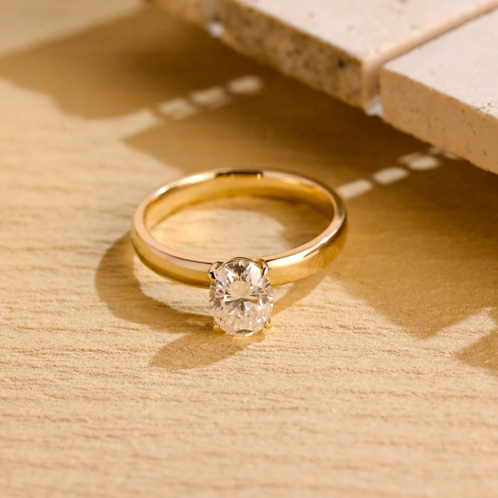 Oval moissanite solitaire engagement ring held by four slim claws on a broad domed polished yellow gold band