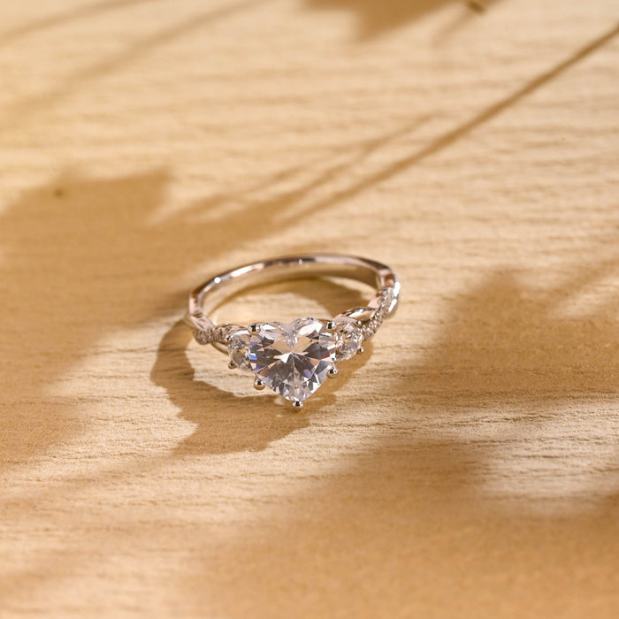 Heart cut moissanite three stone engagement ring with round side stones on a twisted pave set white gold band