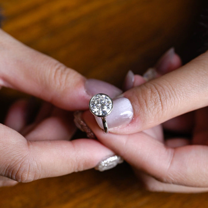 Round moissanite plain bezel solitaire engagement ring with a smooth wide bezel and a plain polished white gold band that tapers up to the stone, view 2