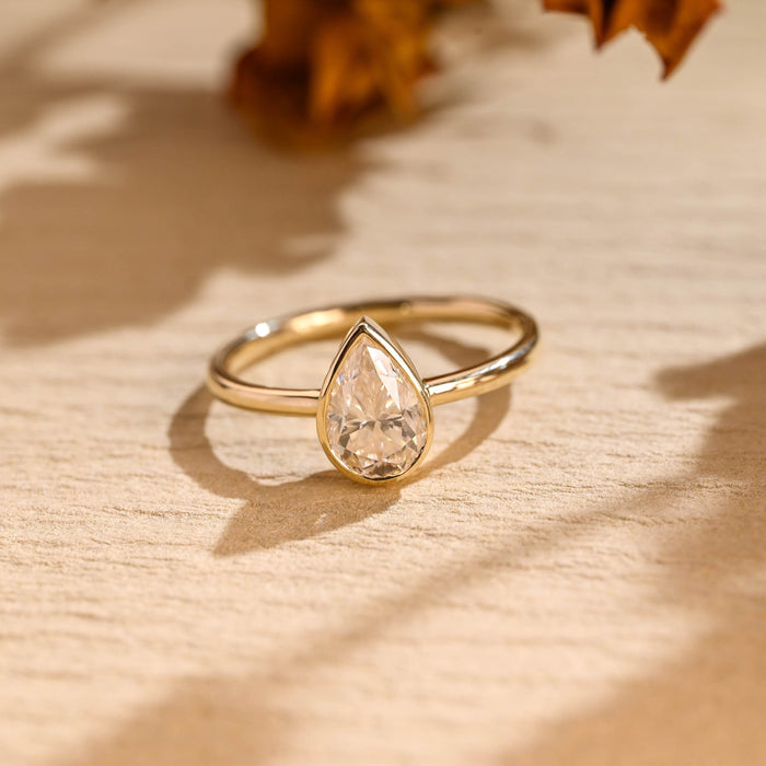 Pear cut moissanite bezel set solitaire engagement ring on a thin polished round yellow gold band