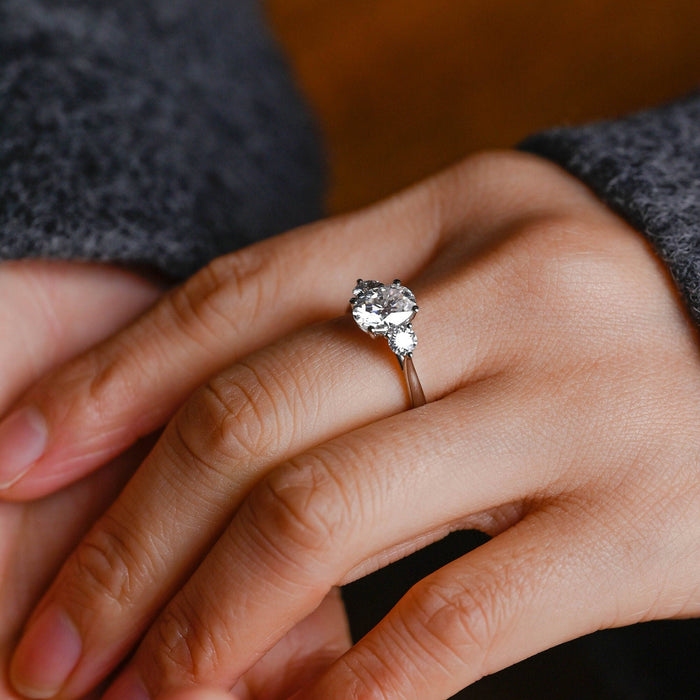Oval moissanite three stone engagement ring with a round stone on each side on a plain polished tapered white gold band, view 2