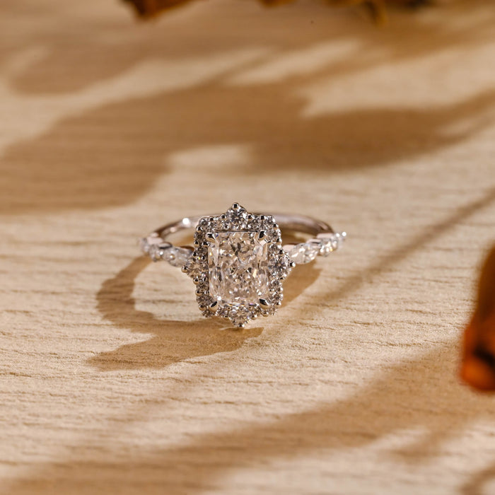 Radiant cut moissanite cluster halo engagement ring with larger round stones at four points and a band of alternating marquise and round stones in white gold