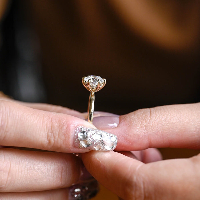 Round moissanite hidden halo engagement ring held by six slim claws on a slim polished yellow gold band, view 2
