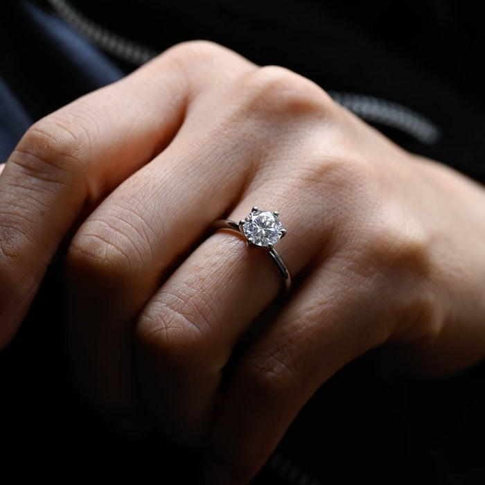 Round moissanite six prong solitaire engagement ring with button tipped prongs on a tapered rounded white gold band, view 2