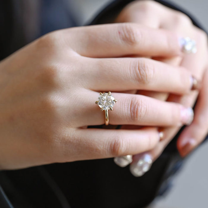Round moissanite six claw solitaire engagement ring with teardrop shaped claws on a fine smooth yellow gold band, view 2