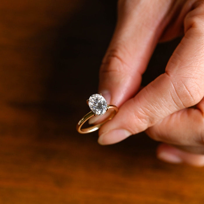 Oval moissanite hidden halo solitaire engagement ring with four claws on a plain polished round yellow gold band, view 2