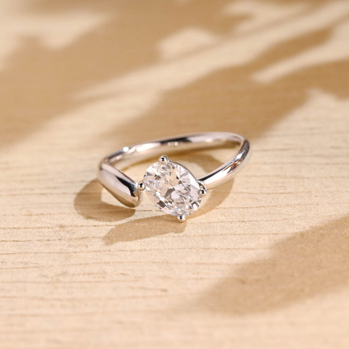 Oval moissanite open shank solitaire engagement ring with the stone tilted in four ball tipped claws on a sweeping polished white gold band
