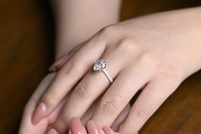 Pear shaped moissanite solitaire engagement ring in claws on a very slim white gold band pave set with tiny round stones, view 2