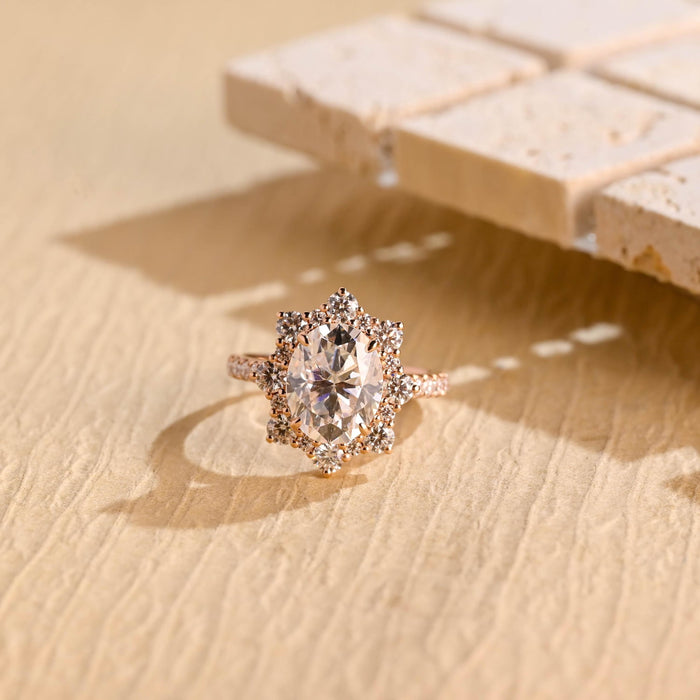 Oval moissanite floral halo engagement ring with a starburst of round stones around the centre stone and a pave set rose gold band