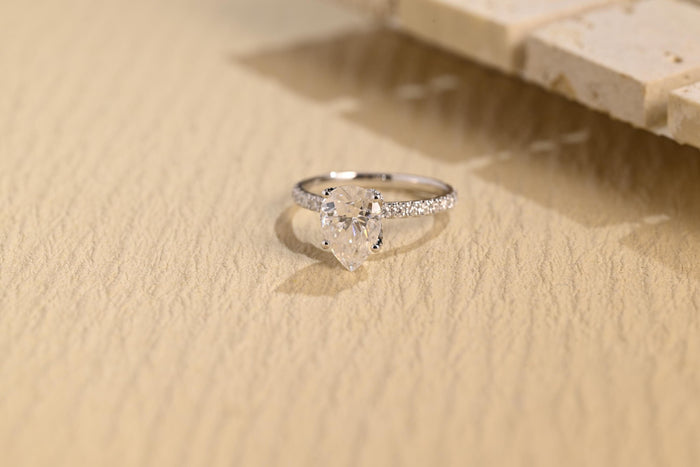 Pear shaped moissanite solitaire engagement ring in claws on a very slim white gold band pave set with tiny round stones