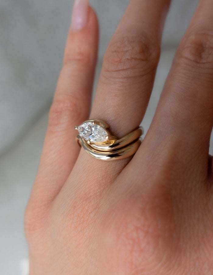 Close-up of four-prong marquise lab grown diamond bypass ring and plain wave band in yellow gold