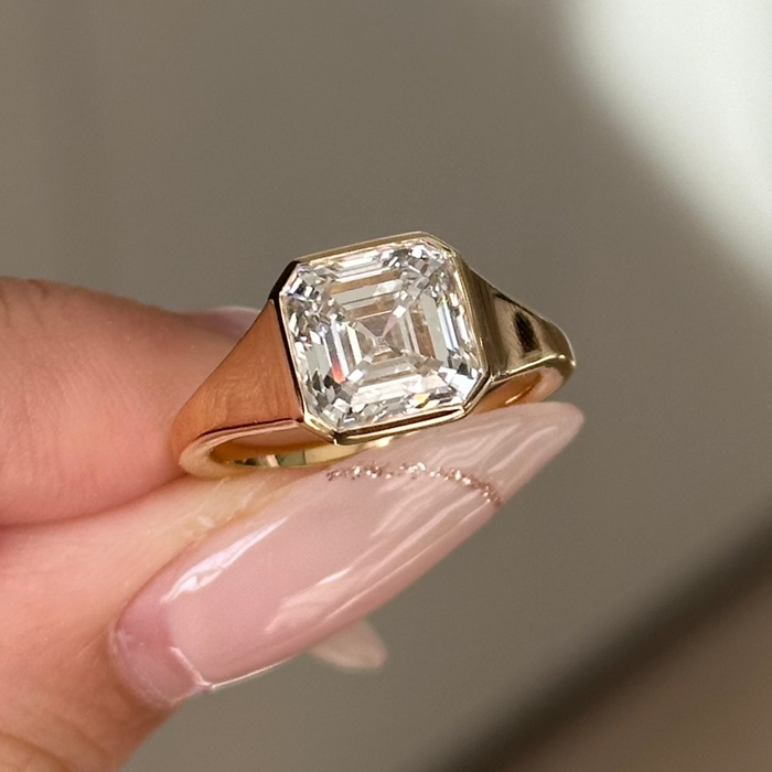 Asscher cut moissanite bezel set engagement ring on a wide tapered yellow gold band