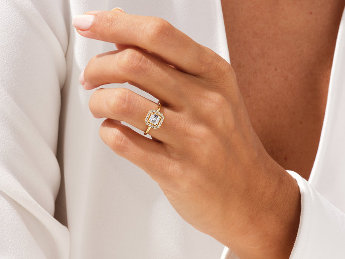 Asscher lab grown diamond micro pave halo ring in yellow gold worn on a raised hand