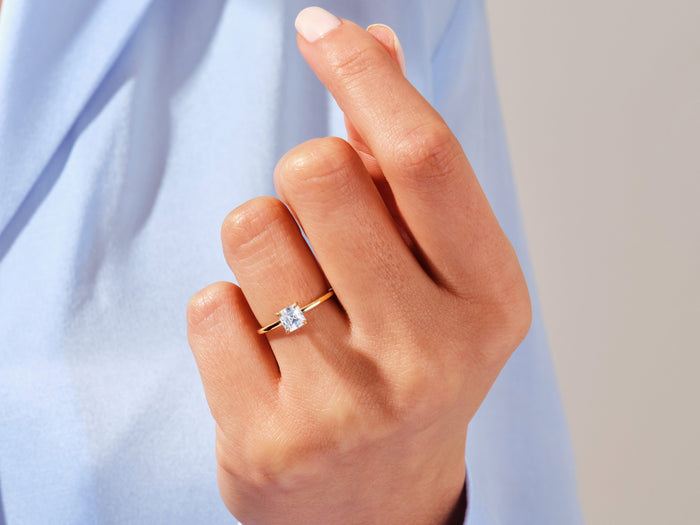 Asscher cut lab grown diamond solitaire ring in yellow gold worn on the ring finger against a blue shirt