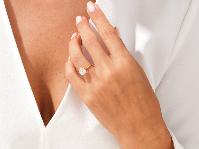 Cushion moissanite bezel engagement ring in yellow gold worn on the ring finger