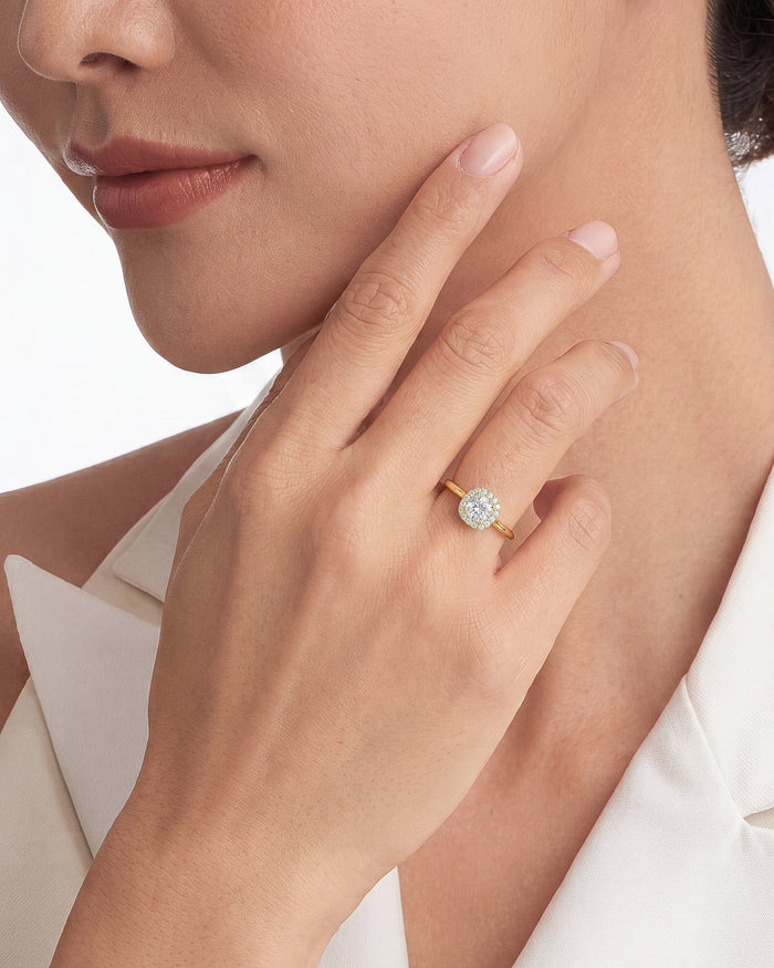 Cushion lab grown diamond halo ring in yellow gold worn on a hand touching the jaw