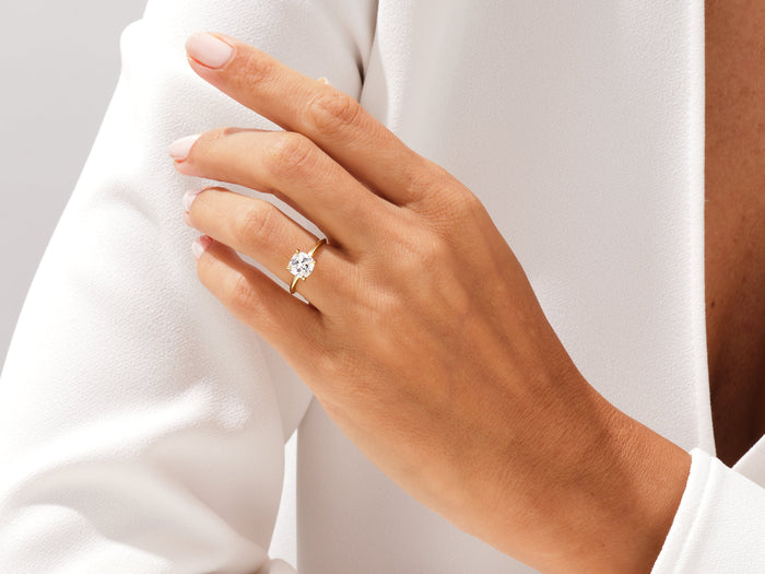 Cushion lab grown diamond knife edge solitaire in yellow gold worn on the hand against a white jacket