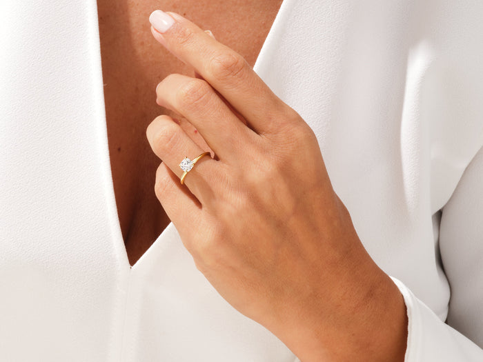 Square cushion lab grown diamond solitaire in yellow gold worn on a hand held near the neckline