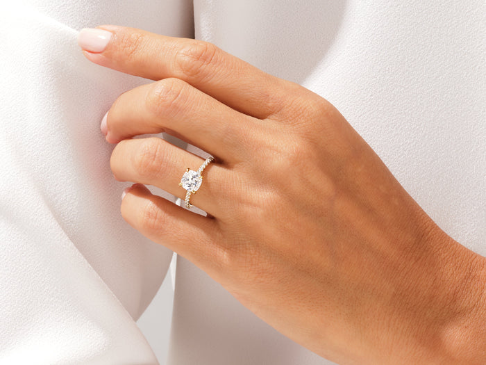 Cushion lab grown diamond pave engagement ring worn on the hand against soft white fabric