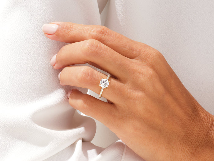 Cushion moissanite pave side stone engagement ring in rose gold worn on the hand