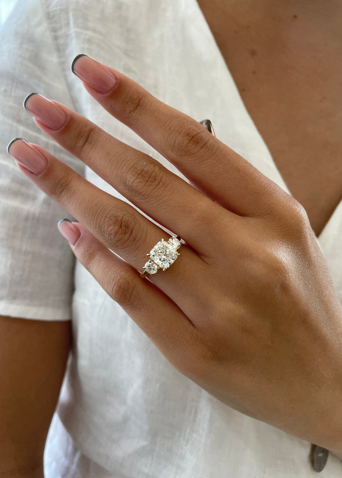 Cushion cut moissanite three stone engagement ring with large round side stones in yellow gold