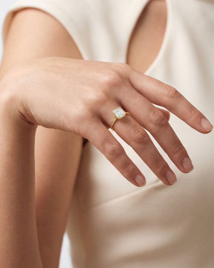 Emerald cut lab grown diamond bezel ring in yellow gold worn on an outstretched hand