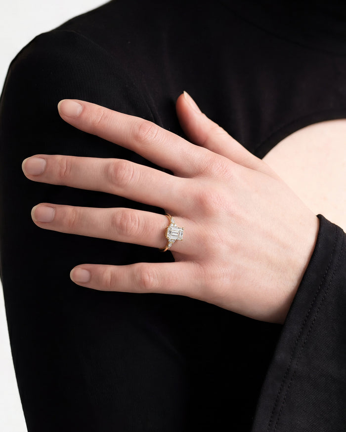 Emerald cut moissanite ring with marquise accents in yellow gold worn on the hand against a black top