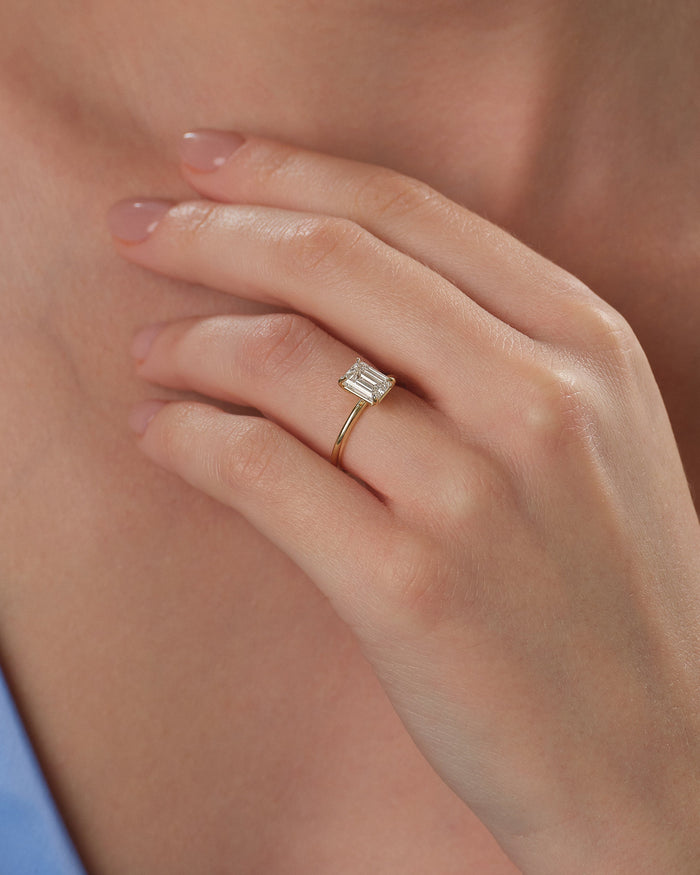 Emerald cut lab grown diamond solitaire in yellow gold worn on the hand at the neckline