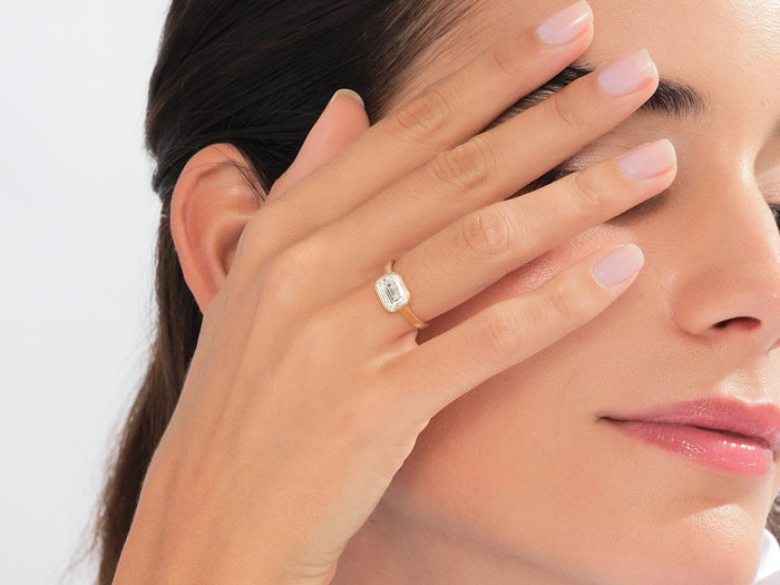 Emerald cut lab grown diamond east west bezel ring in yellow gold worn with the hand over the eye